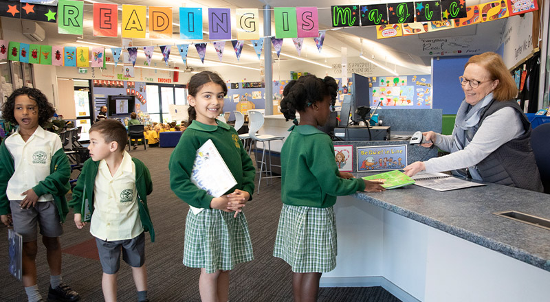 Students lining up to borrow books from the school library at St Mary MacKillop Primary School South Penrith