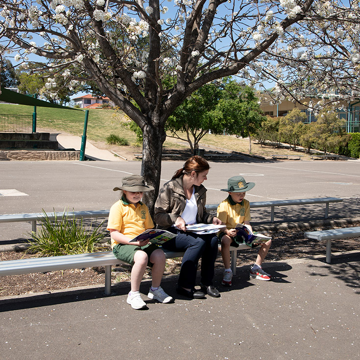 Students reading with their teacher outside under a tree at St Mary MacKillop Primary School South Penrith